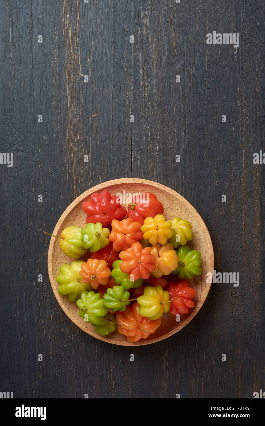 ciliegie suriname, eugenia uniflora, alias pitanga, ciliegia brasiliana o cayenne, frutti colorati e vibranti su piatto di legno, isolati su sfondo rustico nero Foto Stock