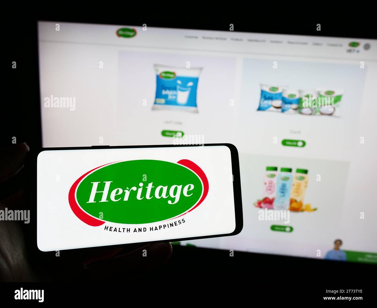 Persona che possiede un telefono cellulare con il logo dell'azienda casearia indiana Heritage Foods Limited davanti alla pagina Web aziendale. Concentrarsi sul display del telefono. Foto Stock