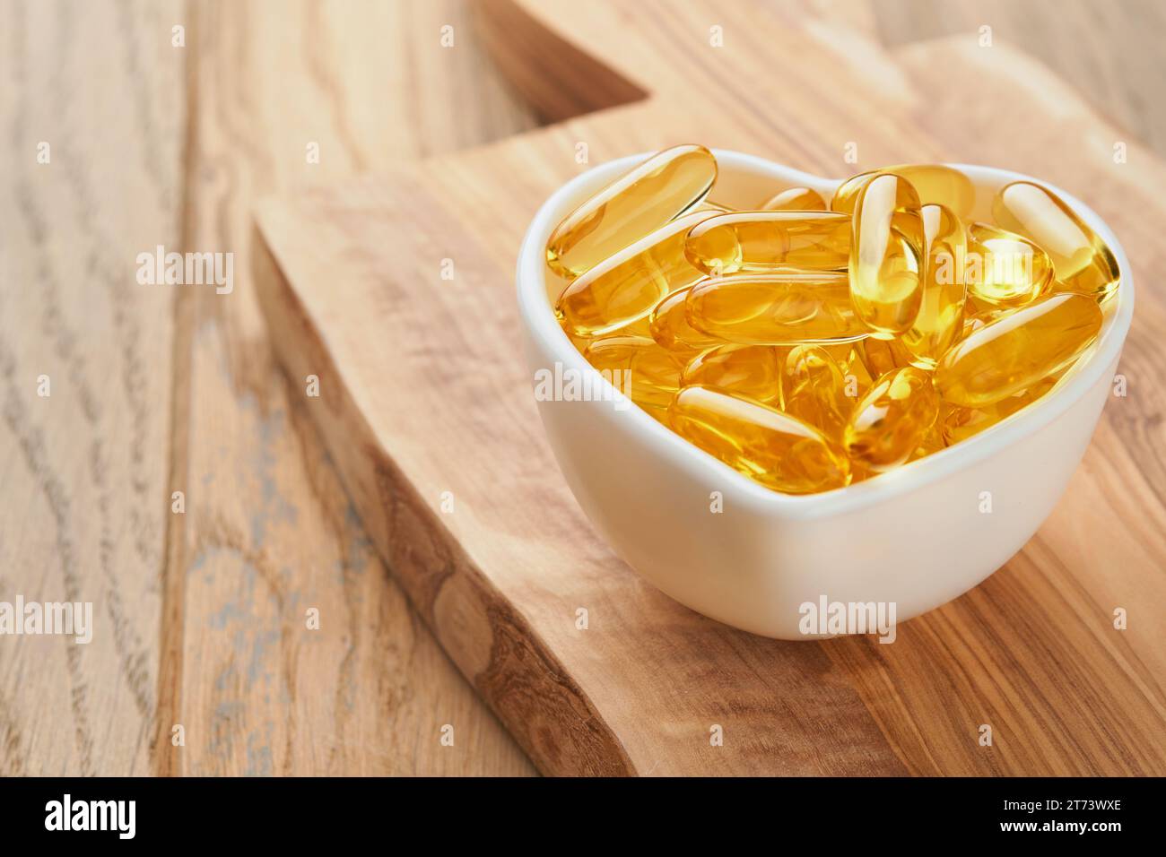 Capsule con vitamina D, e o acidi grassi Omega 3,6,9 in ciotola a forma di cuore su vecchi sfondi di legno. Olio di pesce riempito di olio per integratori alimentari. Supp. Naturale Foto Stock
