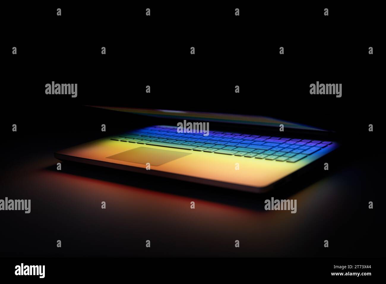notebook mezzo chiuso su un tavolo scuro con riflesso luminoso colorato sulla tastiera Foto Stock