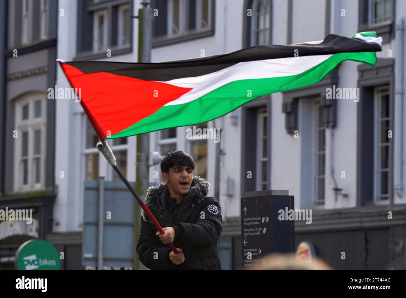 Il giovane musulmano si alza in alto sventolando la sua bandiera alla marcia pro Palestina nel centro di Cardiff, sabato 11 novembre 2023 Foto Stock