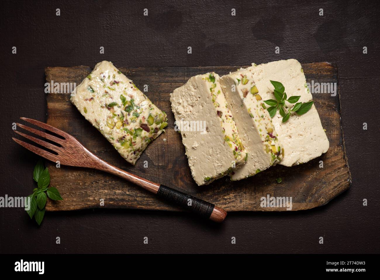 ​​turkish halva tagliata a fette con pistacchio su un piatto di legno e fondo rustico. Dessert orientale tradizionale Foto Stock