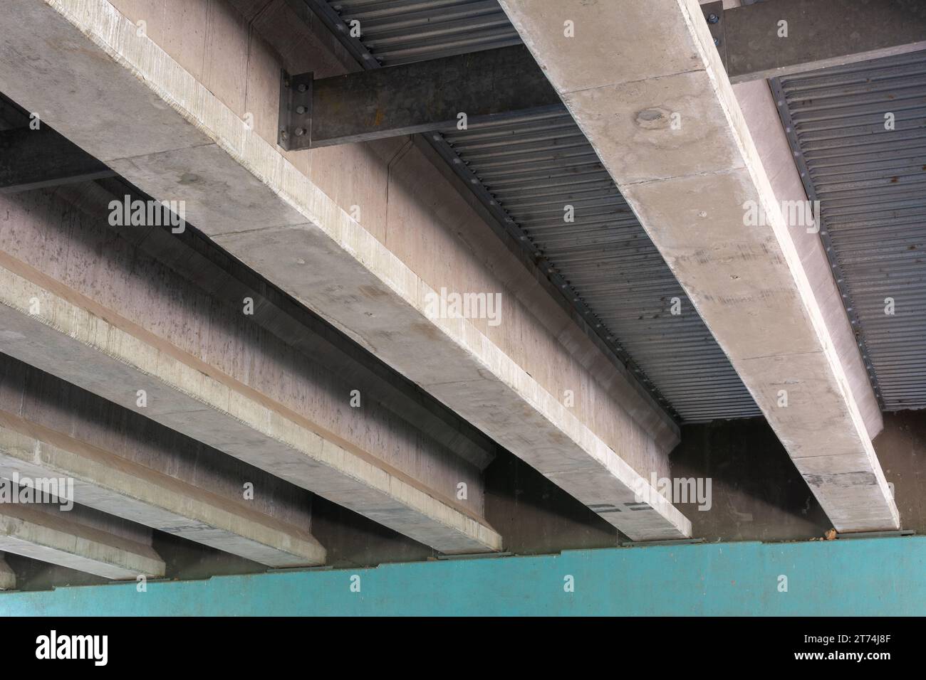 Dettaglio architettonico delle travi di supporto in calcestruzzo sotto un cavalcavia, con lamiere metalliche tra le travi e ombre intense. Foto Stock