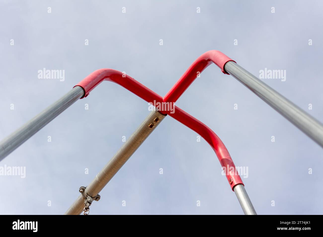 Dettaglio di un'altalena argentata e rossa ambientato su un parco giochi. Un cielo blu pallido pende sopra la testa. Foto Stock