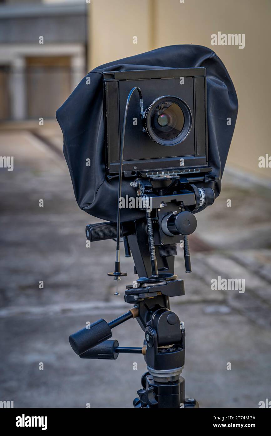 Vista di una fotocamera nera con soffietti fissata a un supporto fotografico in un cortile esterno Foto Stock