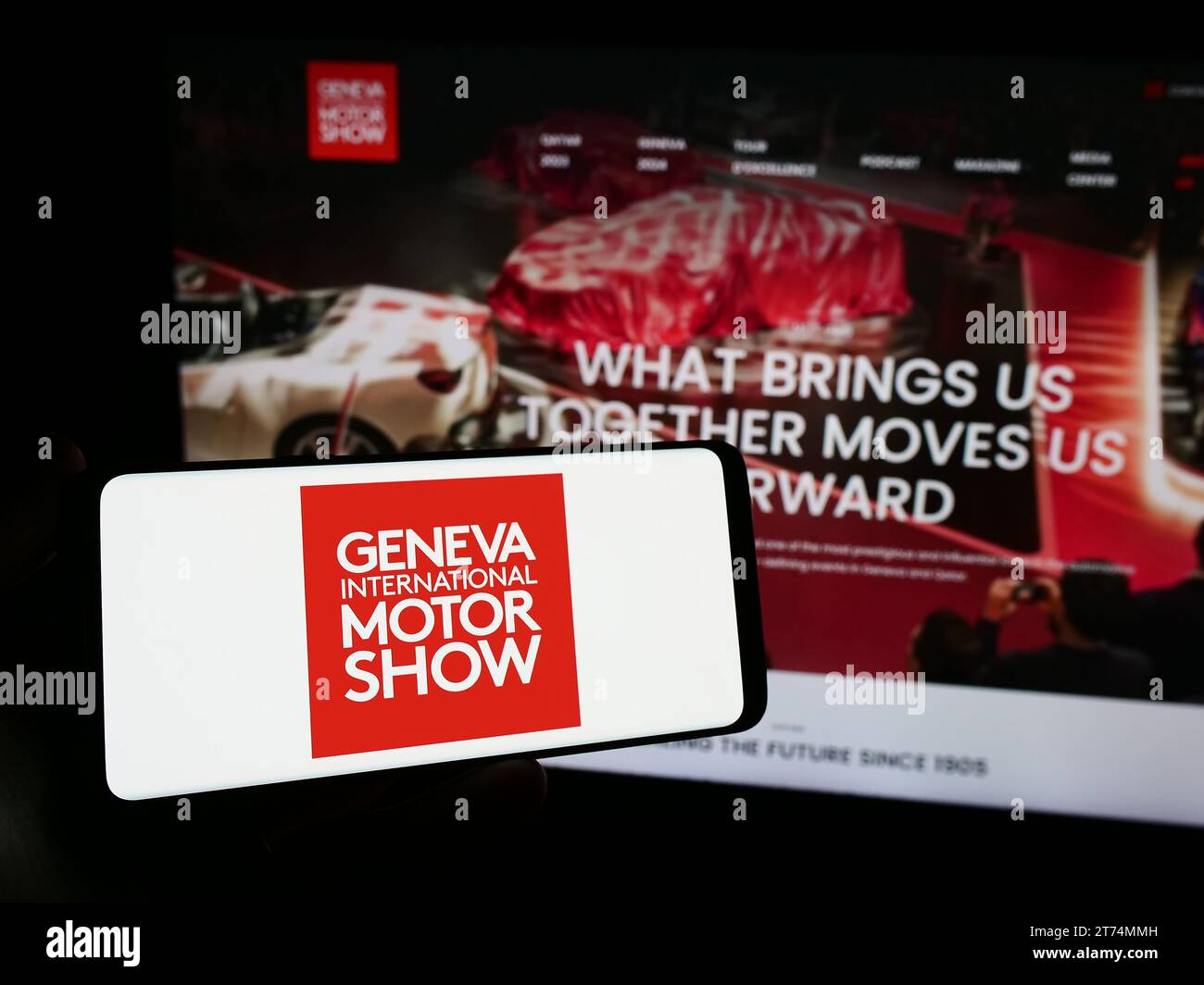 Persona che possiede uno smartphone con il logo del Salone dell'automobile svizzero di Ginevra davanti al sito Web. Concentrarsi sul display del telefono. Foto Stock