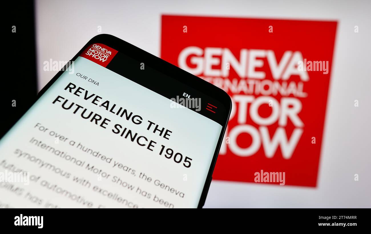 Telefono cellulare con sito Web del Salone dell'automobile svizzero di Ginevra davanti al logo aziendale. Mettere a fuoco in alto a sinistra sul display del telefono. Foto Stock