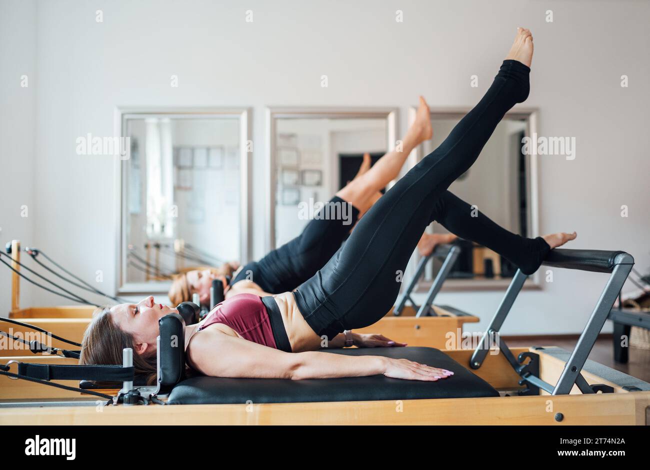 Due femmine in forma fisica che fanno esercizio di bridge con muscoli muscolari del nucleo statico delle gambe sollevate esercitano con la macchina riformatrice pilates nella palestra sportiva sportiva Foto Stock