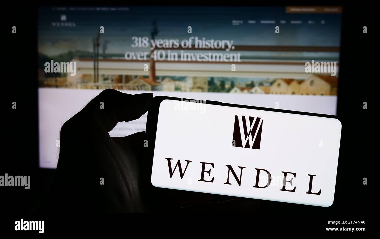Persona in possesso di un cellulare con il logo della società di investimento francese Wendel se davanti alla pagina Web aziendale. Concentrarsi sul display del telefono. Foto Stock