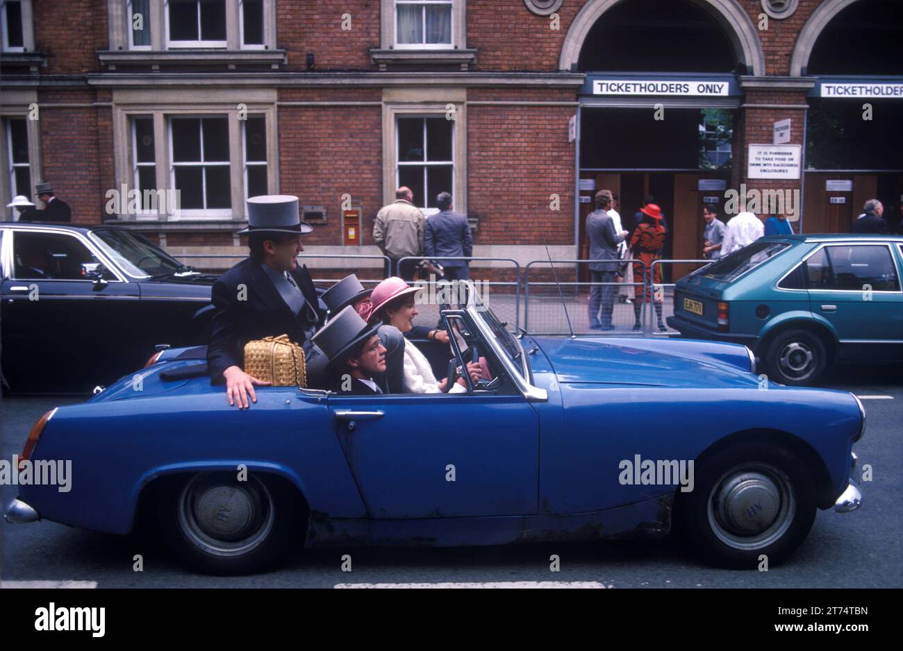 Austin Healey Car 1980s gruppo di persone in auto sportive open top che lasciano le corse di cavalli Royal Ascot. Gli automobilisti se ne vanno dopo una giornata alle corse schiacciate in una vecchia Austin Healey. Ascot, Berkshire, Inghilterra circa giugno 1985. UK HOMER SYKES Foto Stock Austin Healey Car 1980s gruppo di persone in auto sportive open top che lasciano le corse di cavalli Royal Ascot. Gli automobilisti se ne vanno dopo una giornata alle corse schiacciate in una vecchia Austin Healey. Ascot, Berkshire, Inghilterra circa giugno 1985. UK HOMER SYKES Foto Stock