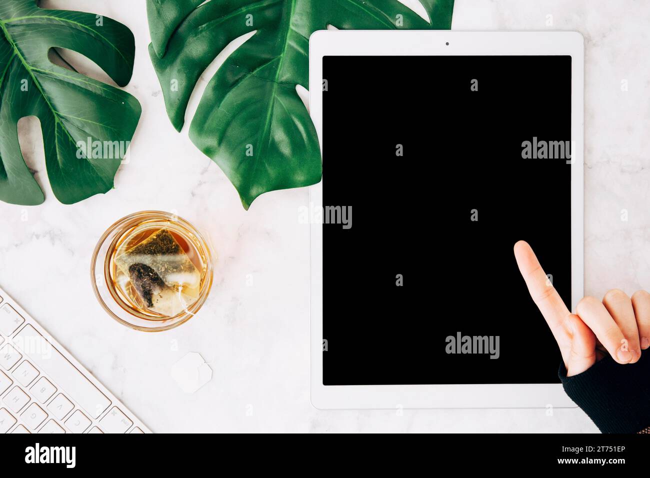 Primo piano: Persona con dito puntato su un tablet digitale con sfondo testurizzato in marmo di vetro del tè Foto Stock