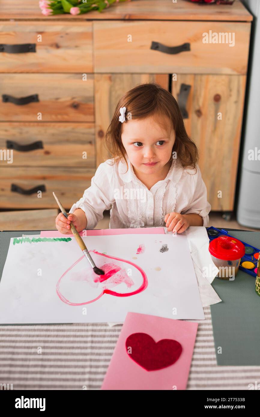 Bambina che dipinge carta per il cuore Foto Stock