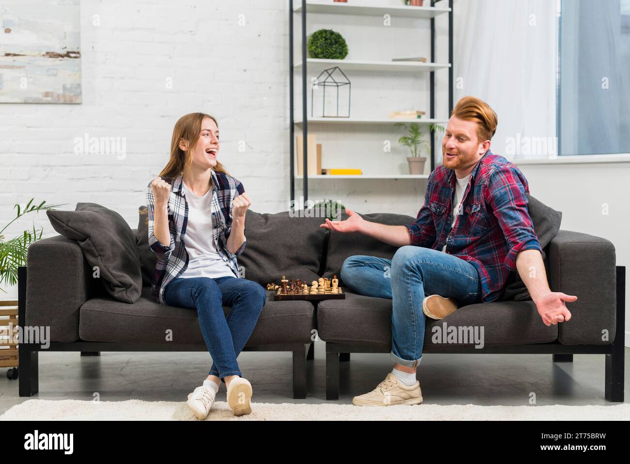 Giovane donna che stringe il pugno con gioia guardando il suo fidanzato che stringe mentre gioca a scacchi Foto Stock