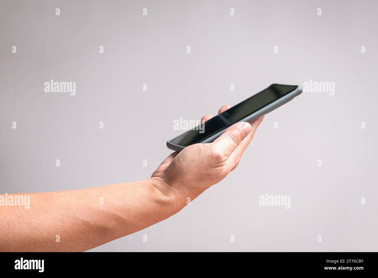 Mano che tiene un telefono, vista laterale. Su sfondo bianco, copia spazio. Foto Stock