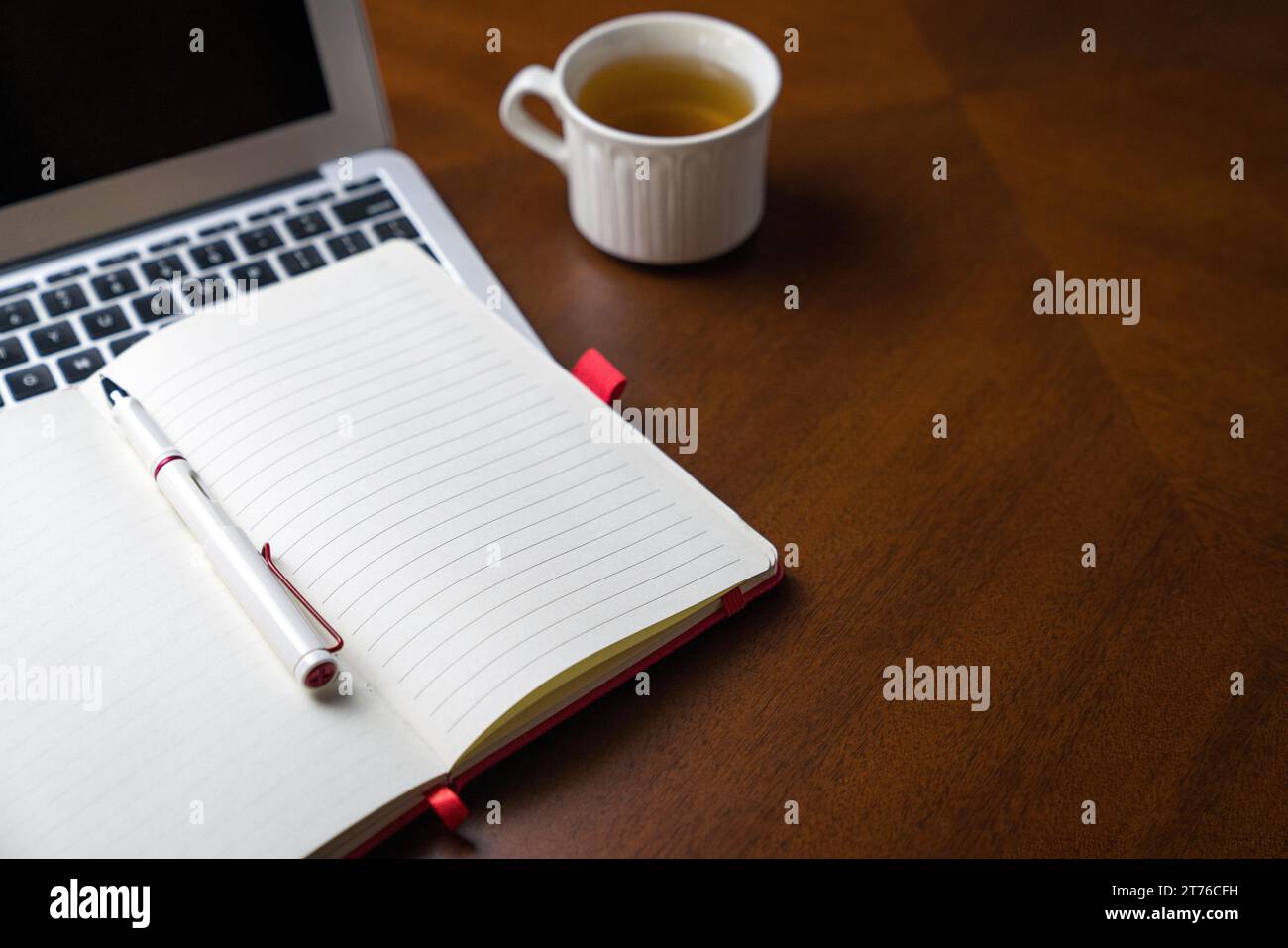 Blocco note sulla parte superiore del notebook e accanto a una tazza di tè. Tavolo in legno, spazio copia. Foto Stock
