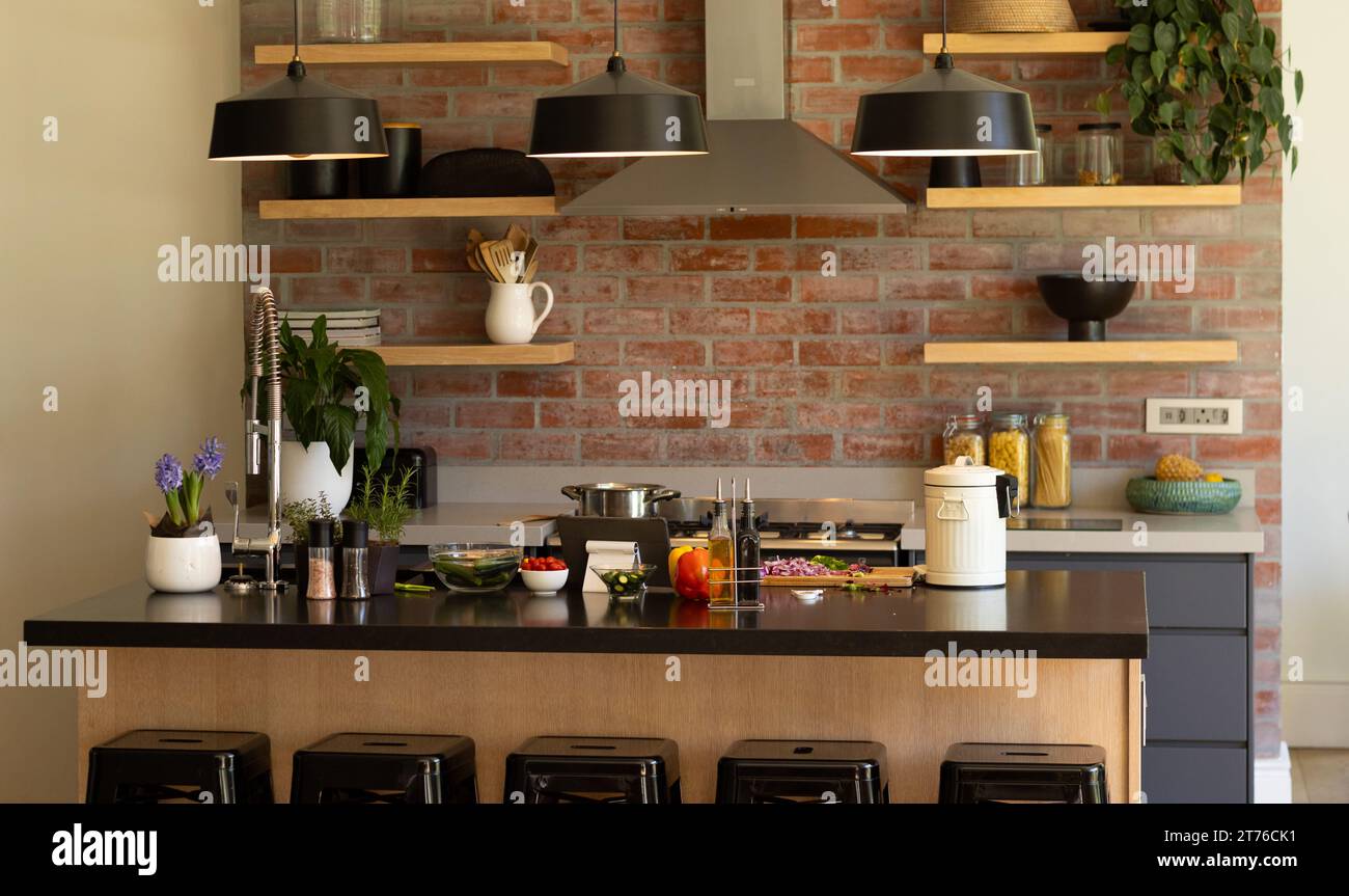 Cucina domestica con mensole e cappuccio sopra il piano cottura su una parete di mattoni a vista e lampade a sospensione sull'isola Foto Stock