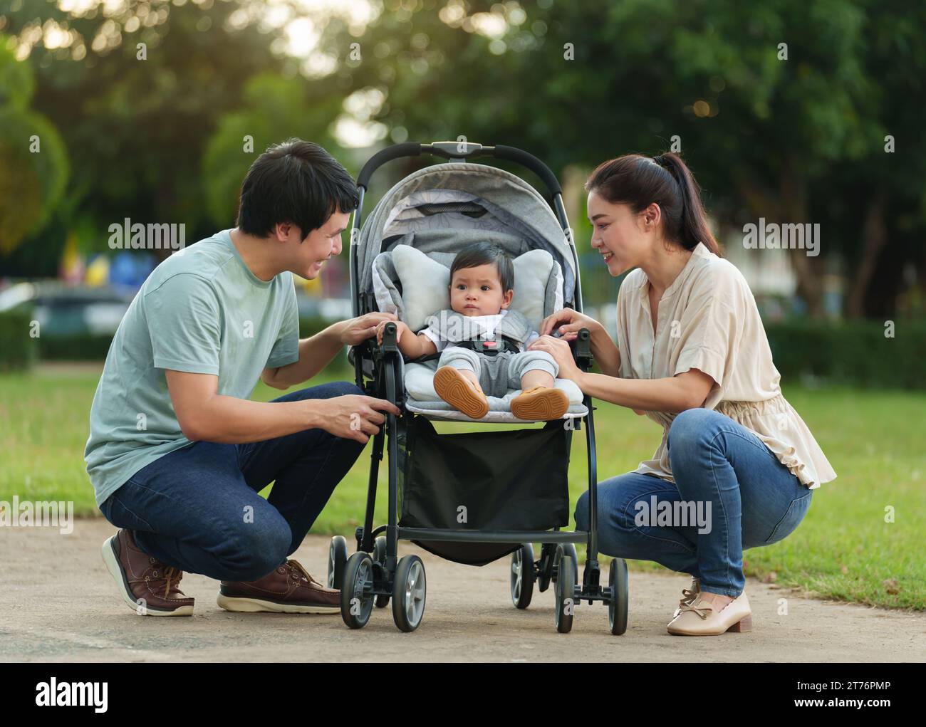 genitore felice (padre e madre) che parla e gioca con il bambino nel passeggino mentre riposa nel parco Foto Stock