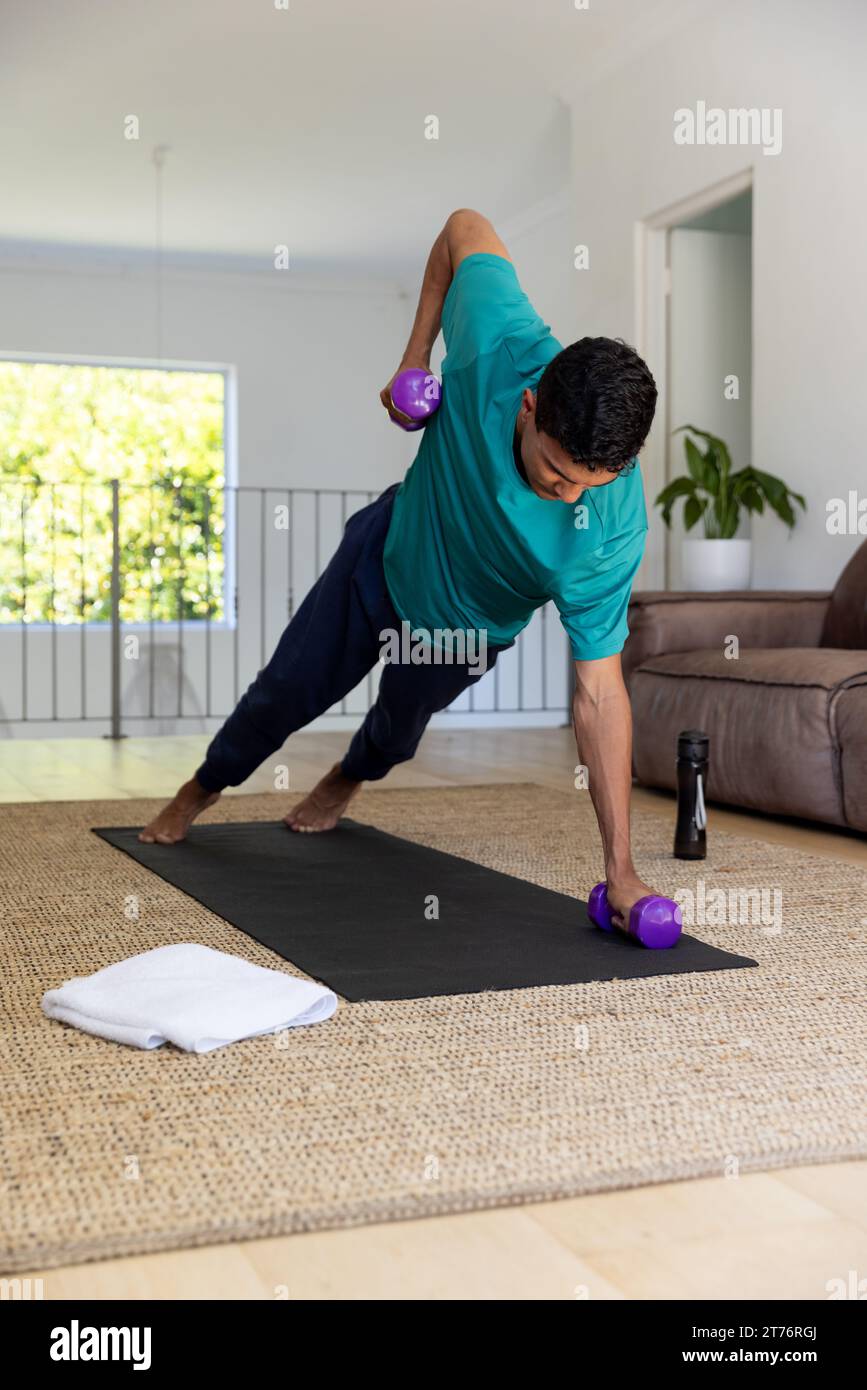 Uomo birazziale che fa esercizio con manubri sul tappeto a casa Foto Stock