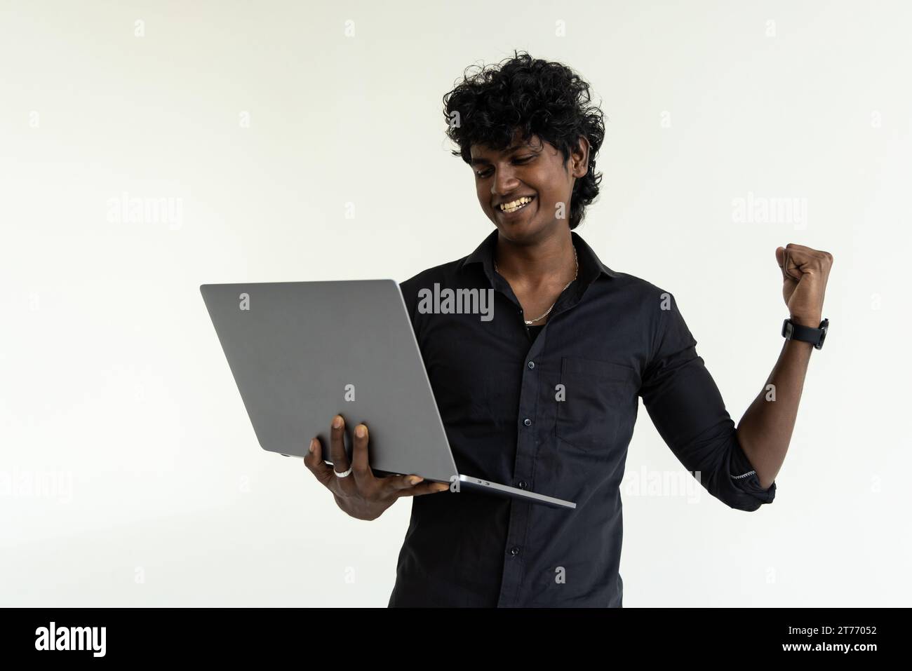 Felice entusiasta imprenditore indiano dipendente che tiene un computer portatile isolato su sfondo grigio per celebrare la vittoria, buoni risultati online, affari Foto Stock