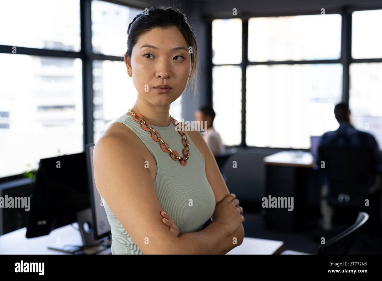 Donna d'affari asiatica informale e seria, con le braccia incrociate dalla scrivania in ufficio, nello spazio fotocopie Foto Stock