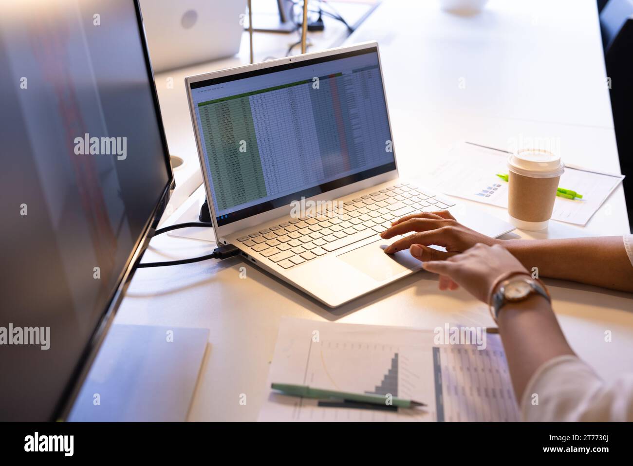Mani di una donna d'affari birazziale che usa lo schermo di un computer portatile e uno schermo di un computer alla scrivania dell'ufficio Foto Stock