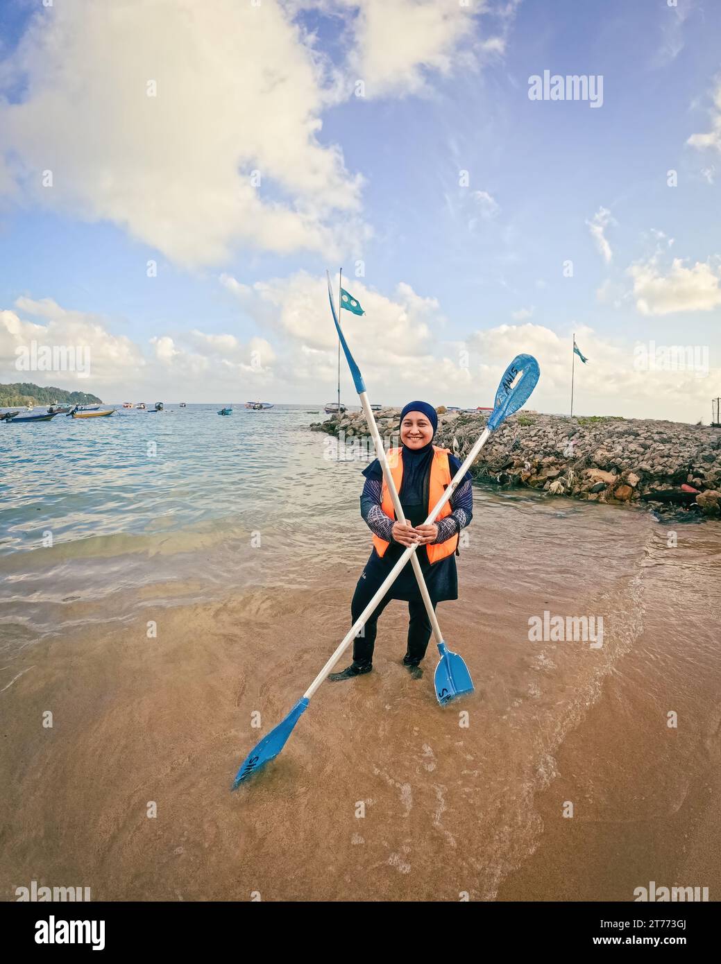 La donna musulmana che indossa burqini e giubbotto salvagente tiene la pagaia in kayak vicino alla spiaggia di un'isola. Foto Stock