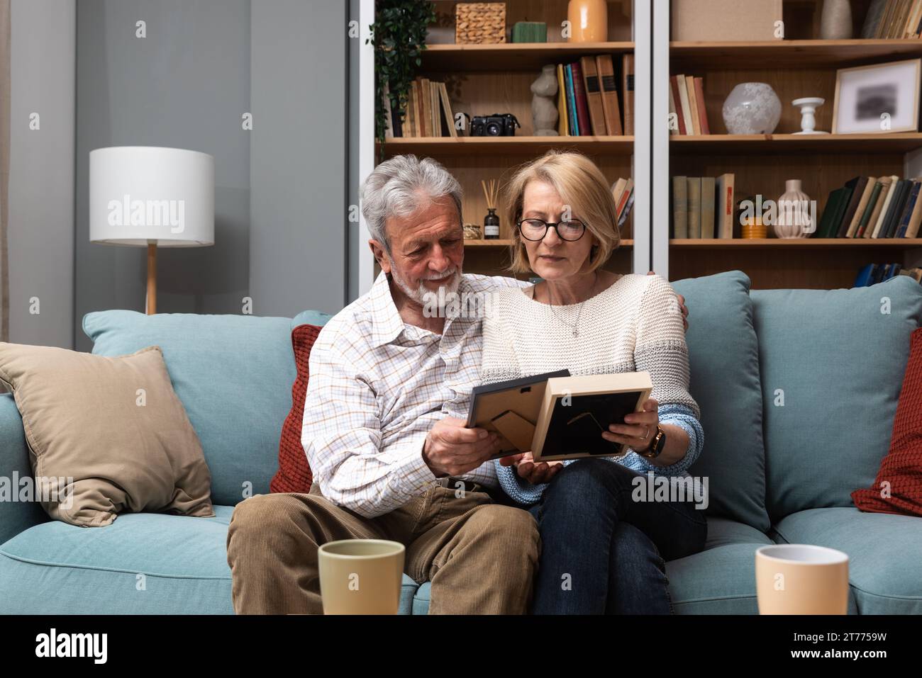 Due anziani coppia uomo e donna che guardano una foto di famiglia sorridere e abbracciare mentre si siede a casa sul divano. ricordi e nostalgia per il bambino Foto Stock