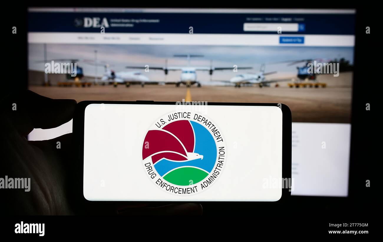 Persona in possesso di cellulare con sigillo della United States Drug Enforcement Administration (DEA) davanti alla pagina web. Concentrarsi sul display del telefono. Foto Stock