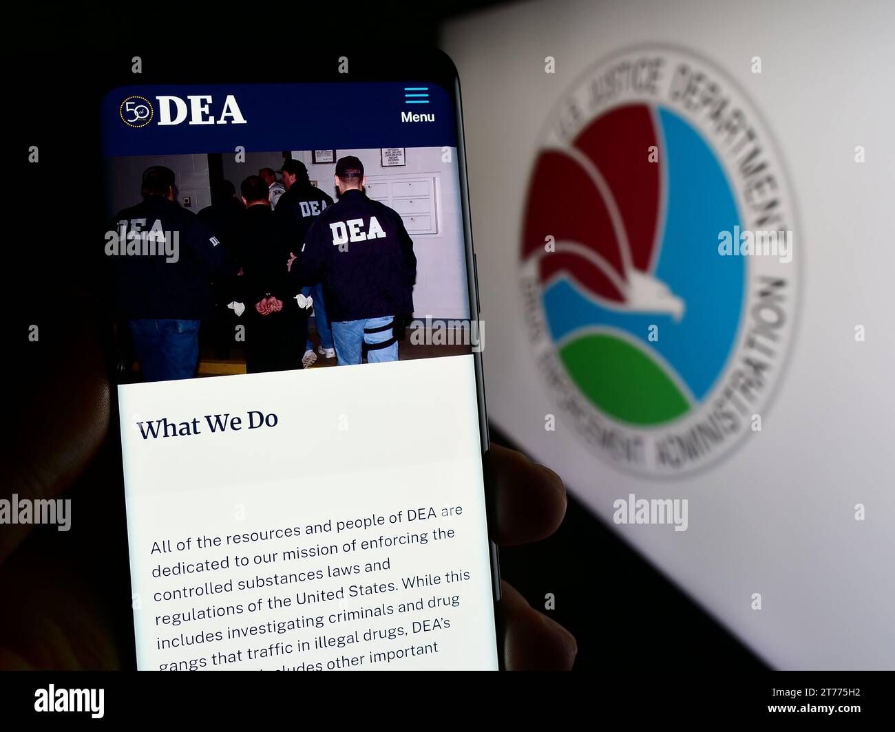 Persona in possesso di un cellulare con la pagina web della United States Drug Enforcement Administration (DEA) davanti al sigillo. Concentrarsi sul centro del display del telefono. Foto Stock