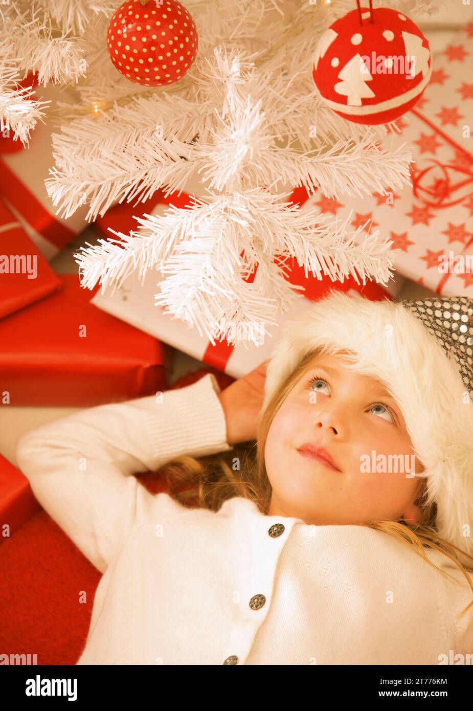 Ragazza sdraiata sotto un albero di Natale rosso e bianco che guarda in alto Foto Stock