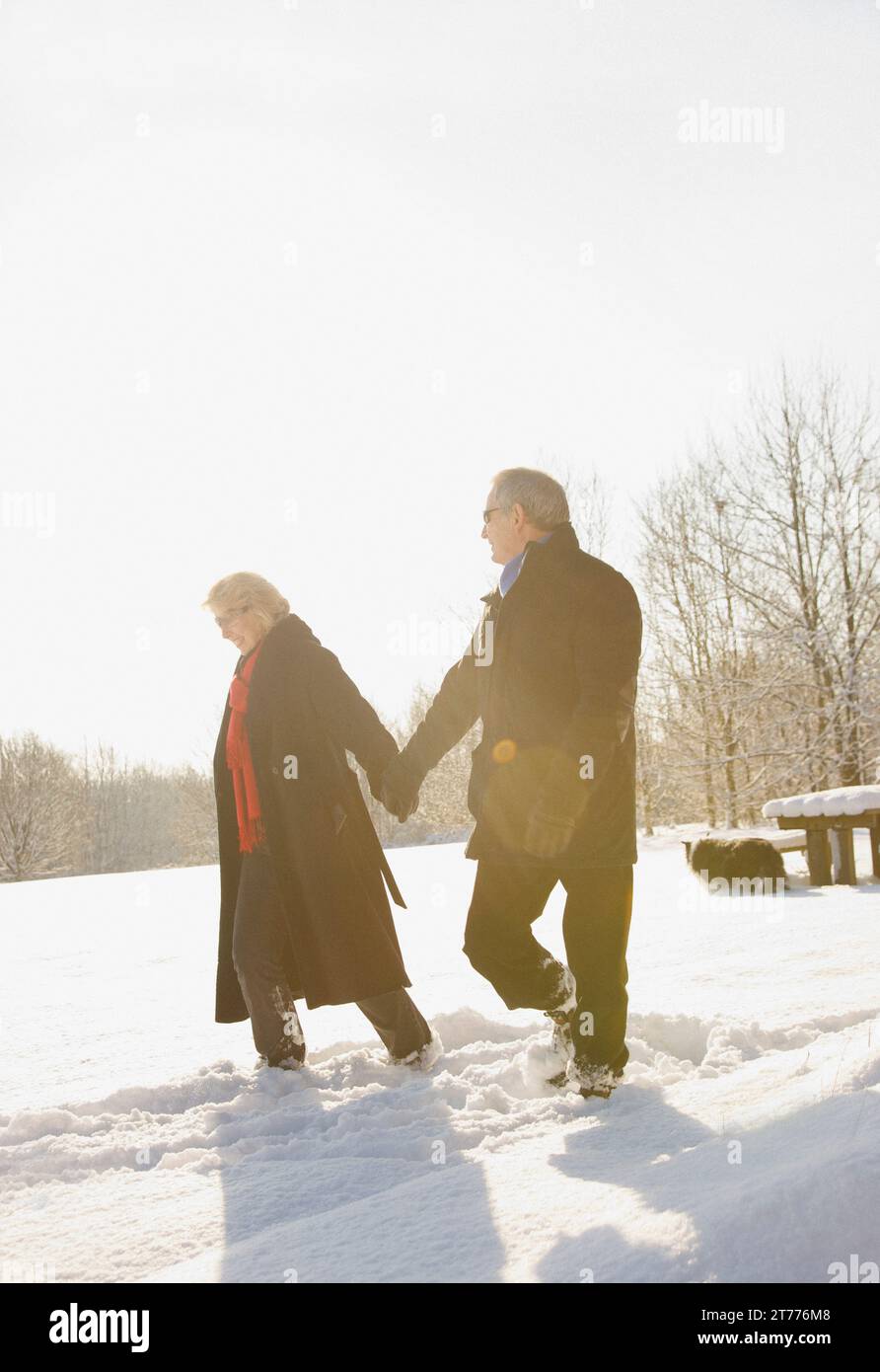 Coppia matura passeggiate nella neve tenendo le mani Foto Stock