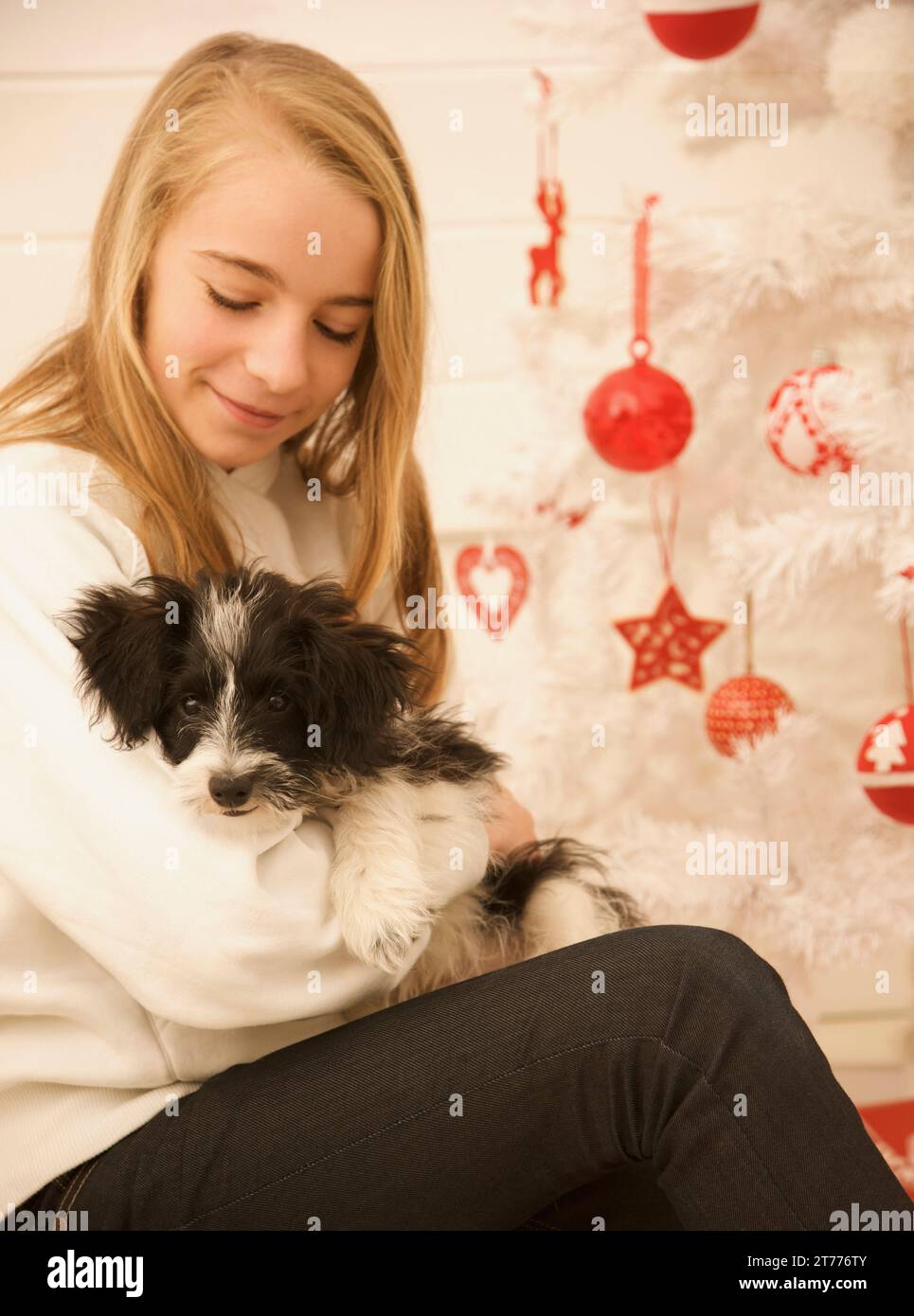 Giovane ragazza seduta da un albero di Natale tenendo un cucciolo Foto Stock