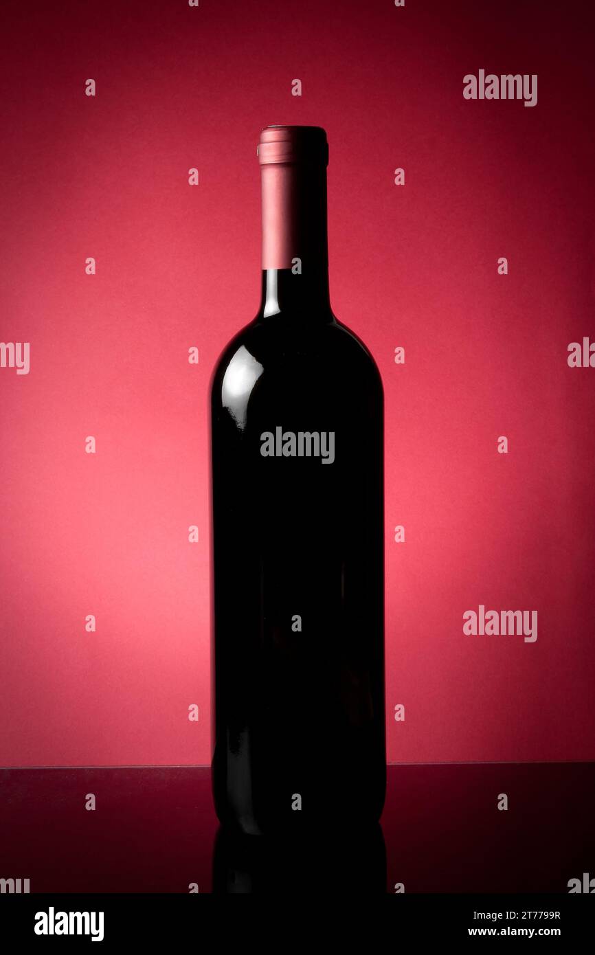 bottiglia di vino rosso su tavola nera e fondo rosso Foto Stock