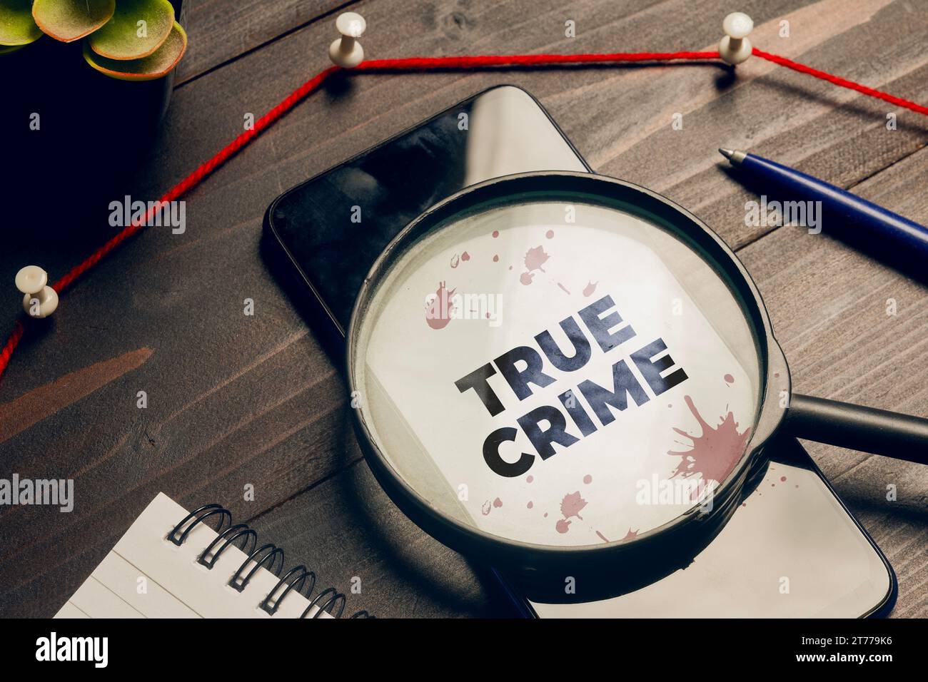 True Crime Concept: Una lente di ingrandimento sopra uno smartphone sulla scrivania di un detective Foto Stock