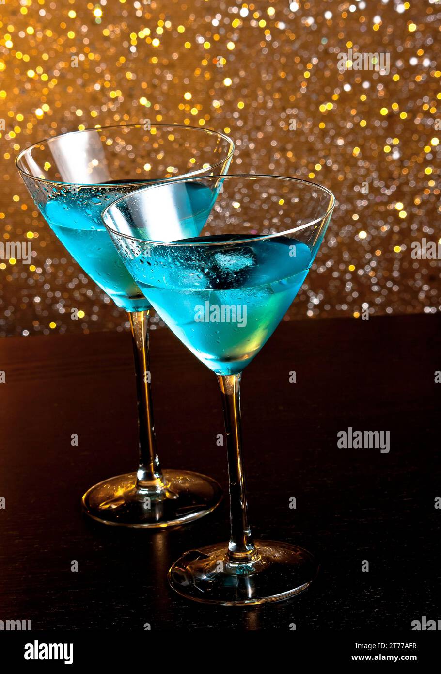 due bicchieri di fresco cocktail blu con ghiaccio su sfondo bokeh chiaro e dorato su un tavolo di legno Foto Stock