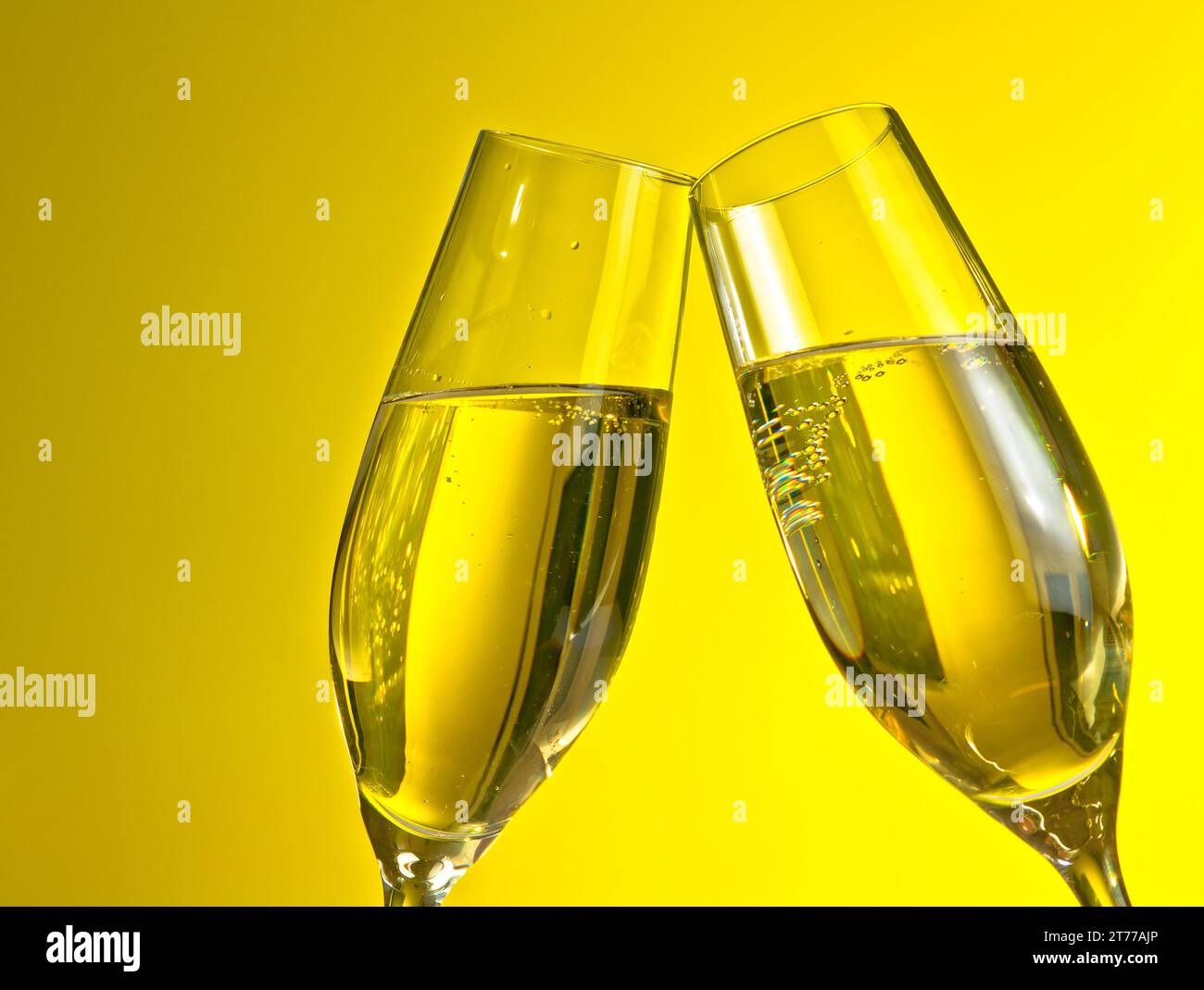 un paio di flauti di champagne con bolle d'oro fanno il tifo su sfondo giallo chiaro con spazio per il testo Foto Stock