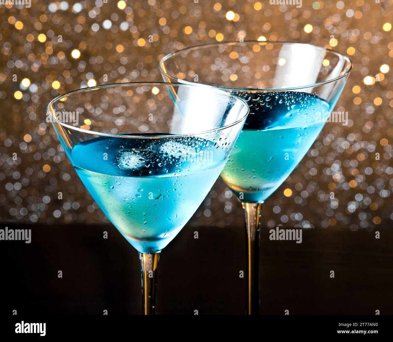 due bicchieri di fresco cocktail blu con ghiaccio su sfondo bokeh chiaro e dorato su un tavolo di legno Foto Stock
