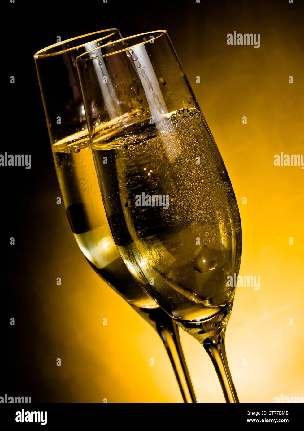 un paio di flute di champagne con bolle d'oro su sfondo chiaro dorato scuro con spazio per il testo Foto Stock