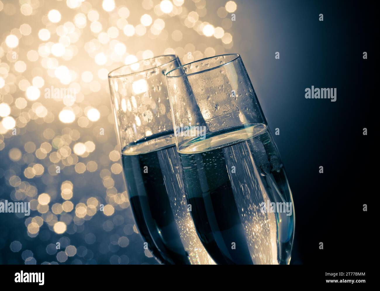 dettaglio di flauti di champagne con bolle dorate su sfondo bokeh chiaro blu scuro con spazio per il testo Foto Stock