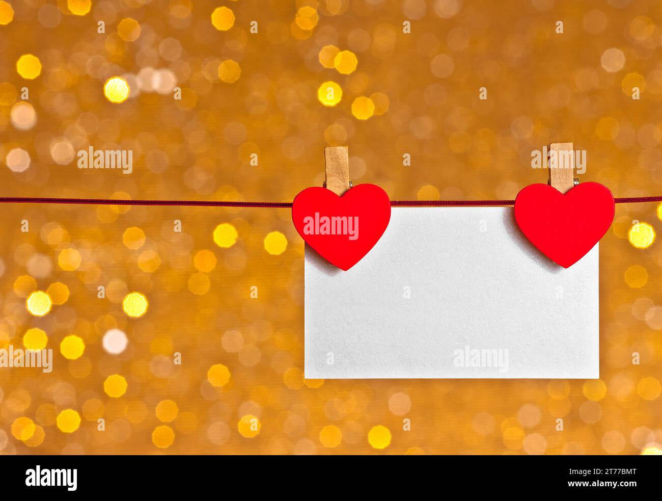 due cuori decorativi rossi con biglietto d'auguri appeso su sfondo bokeh chiaro dorato con spazio per il testo, concetto di san valentino Foto Stock
