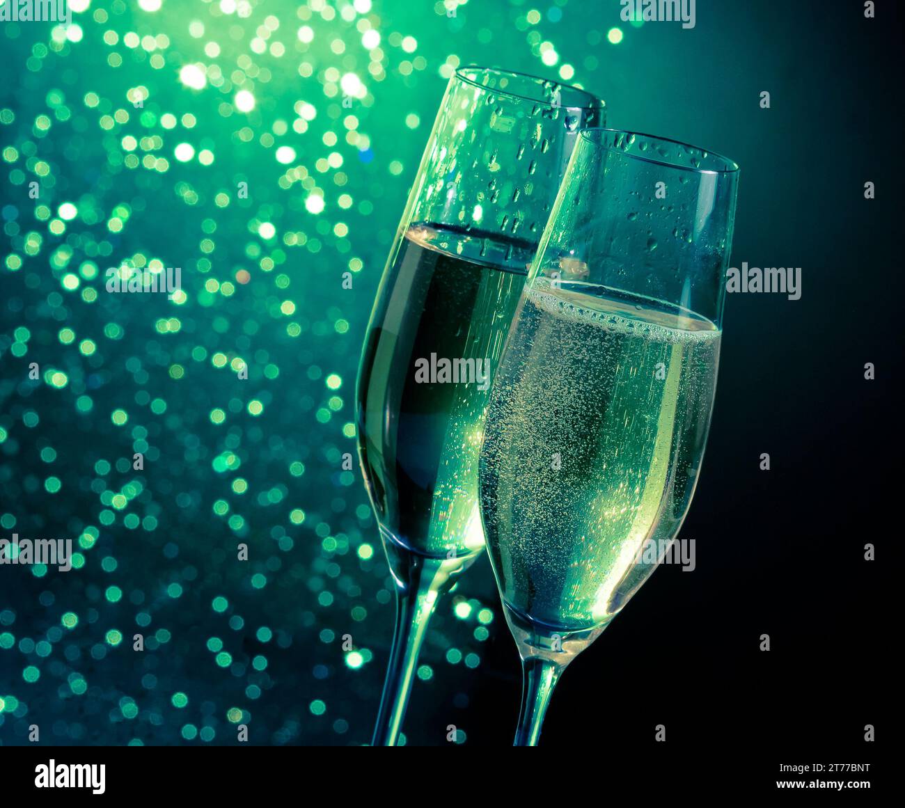 Champagne flauti con bolle d'oro su verde scuro luce sfondo bokeh di fondo con spazio per il testo Foto Stock