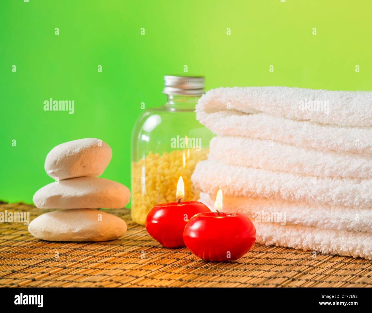 Massaggio spa con sfondo bordo con asciugamano impilato, candele rosse e pietra su sfondo verde bokeh Foto Stock