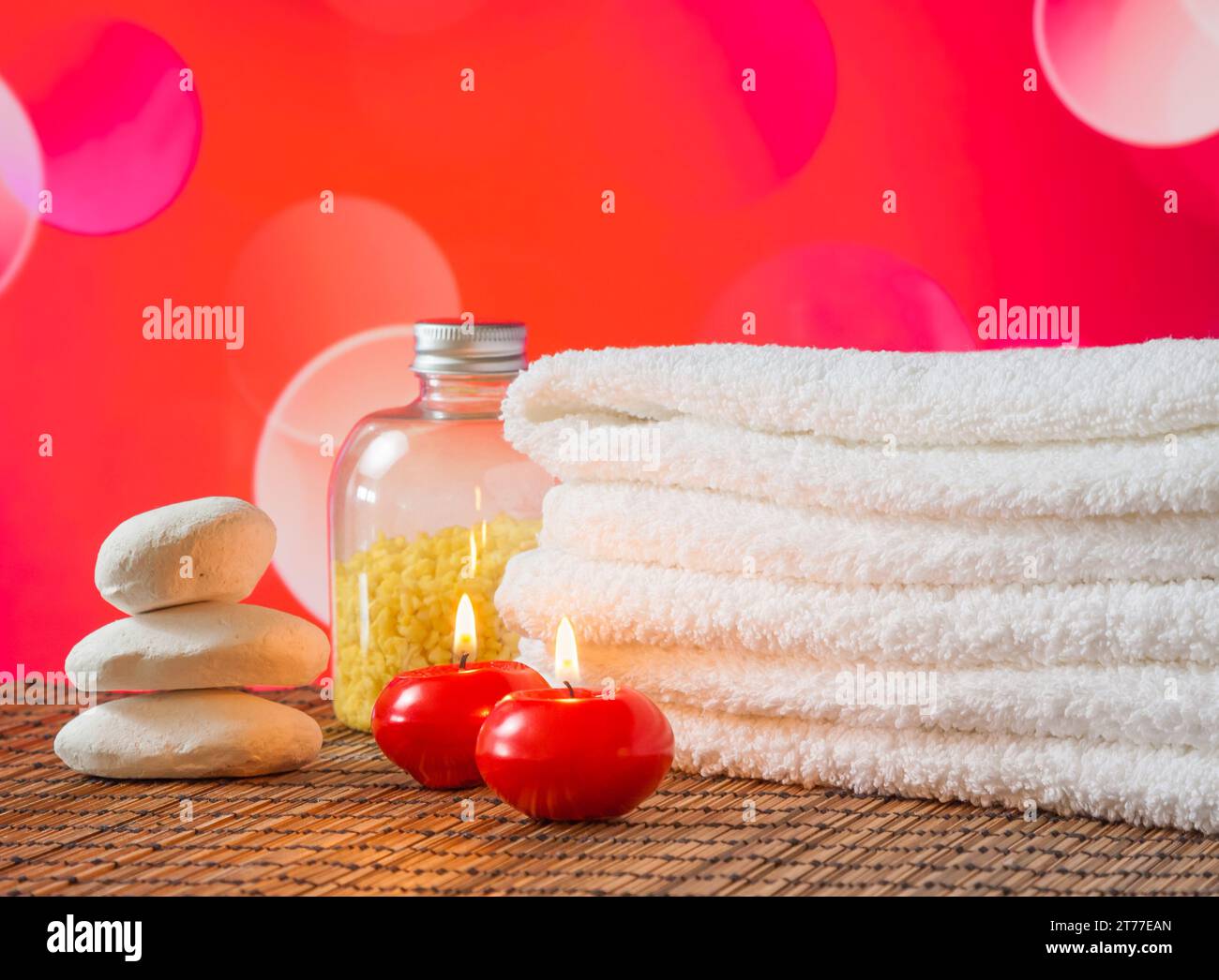 Massaggio spa con asciugamano impilato, candele rosse e pietra su sfondo bokeh rosso per san valentino Foto Stock