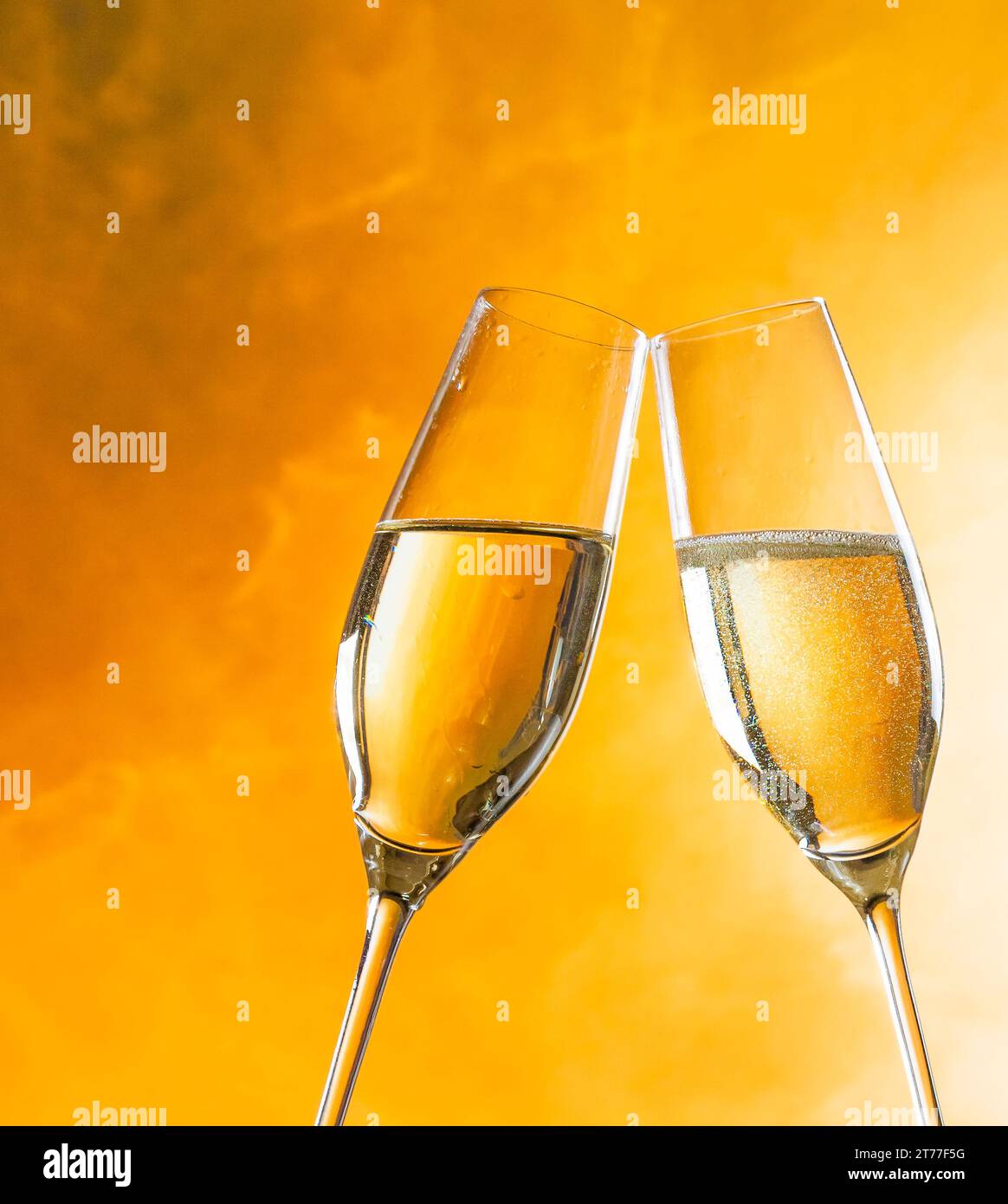 un paio di flauti di champagne con bolle d'oro fanno il tifo su sfondo chiaro dorato con spazio per il testo Foto Stock