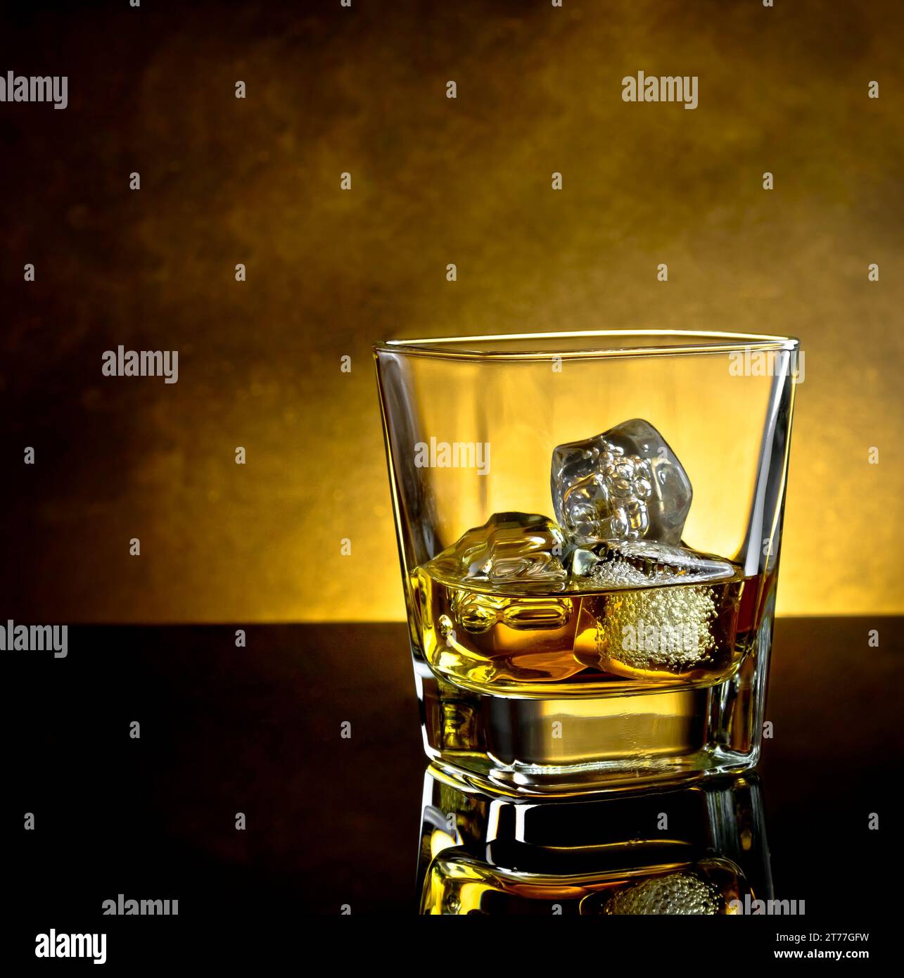 bicchiere di whisky con ghiaccio e luce calda su un tavolo nero con riflessi e atmosfera calda Foto Stock