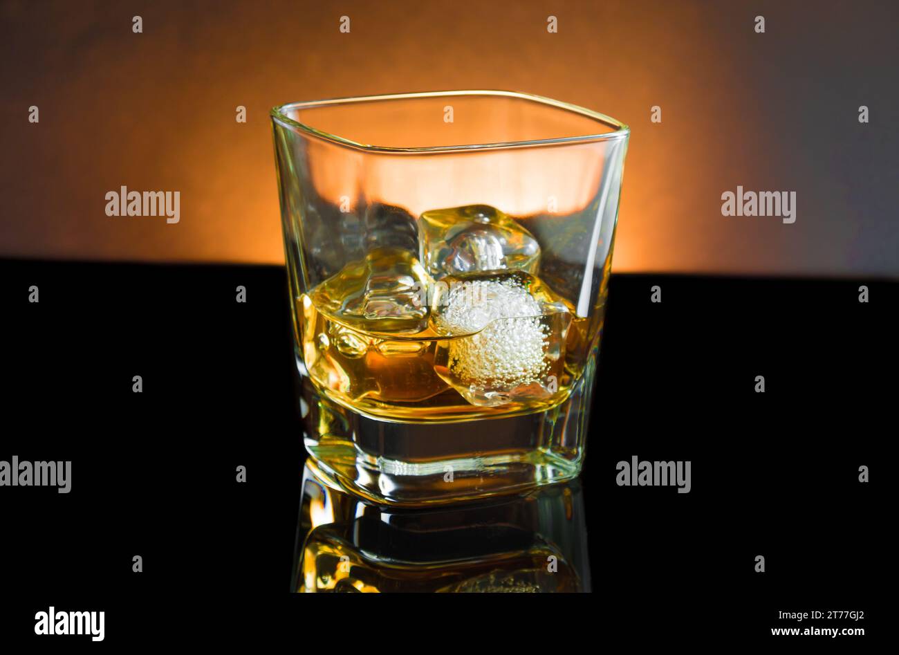 bicchiere di whisky con ghiaccio e luce calda su sfondo nero, con riflesso Foto Stock