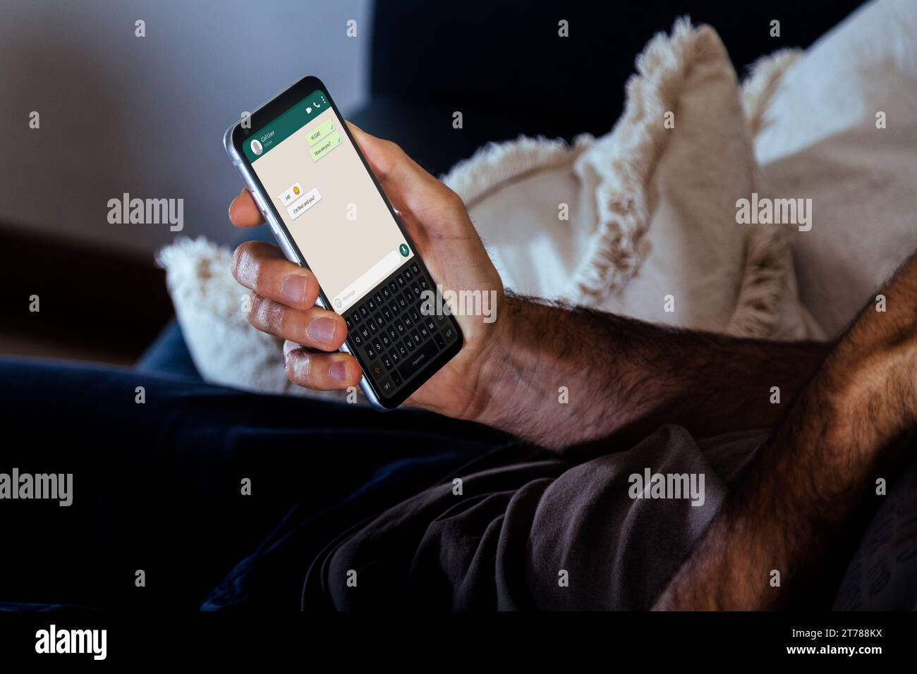 Uomo che riposa su un divano tenendo in mano un cellulare con un'app di chat sullo schermo. Invio di messaggi tramite smartphone. Foto Stock