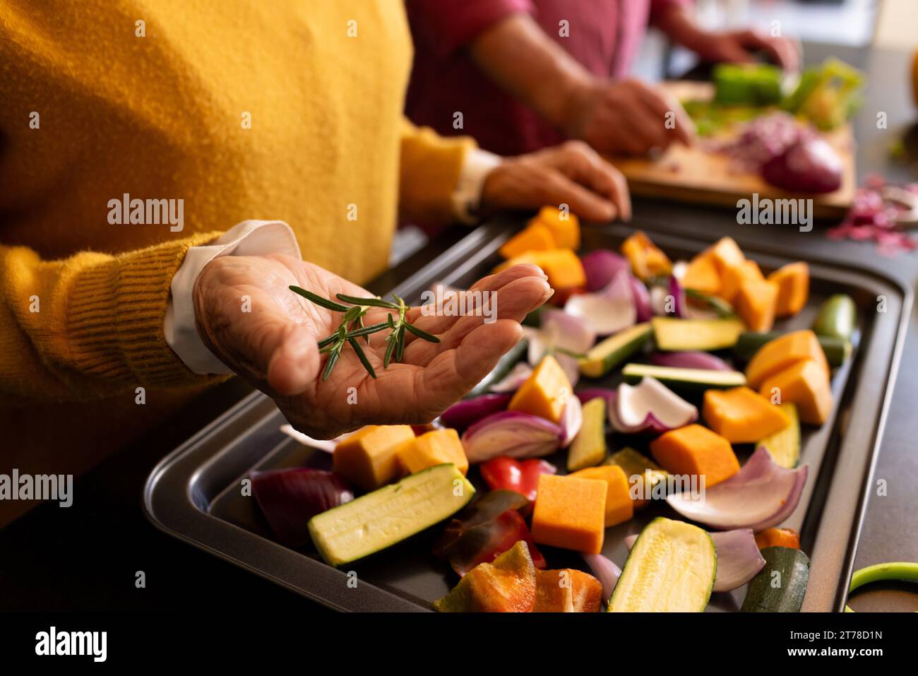 Parte centrale della coppia caucasica senior che prepara verdure, condimento con rosmarino fresco Foto Stock