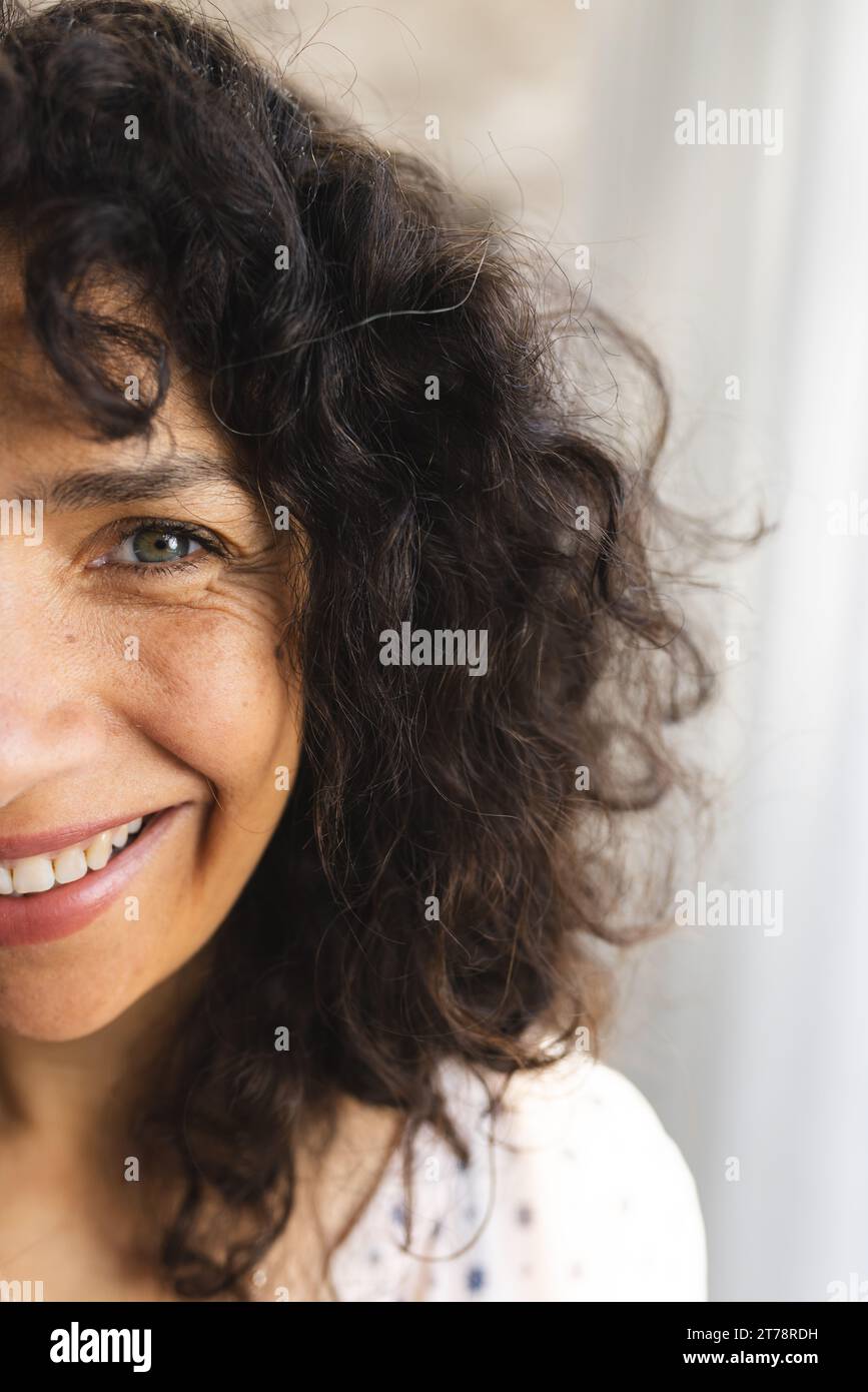 Metà ritratto di donna matura caucasica felice con lunghi capelli ricci scuri, sorridente al sole a casa Foto Stock