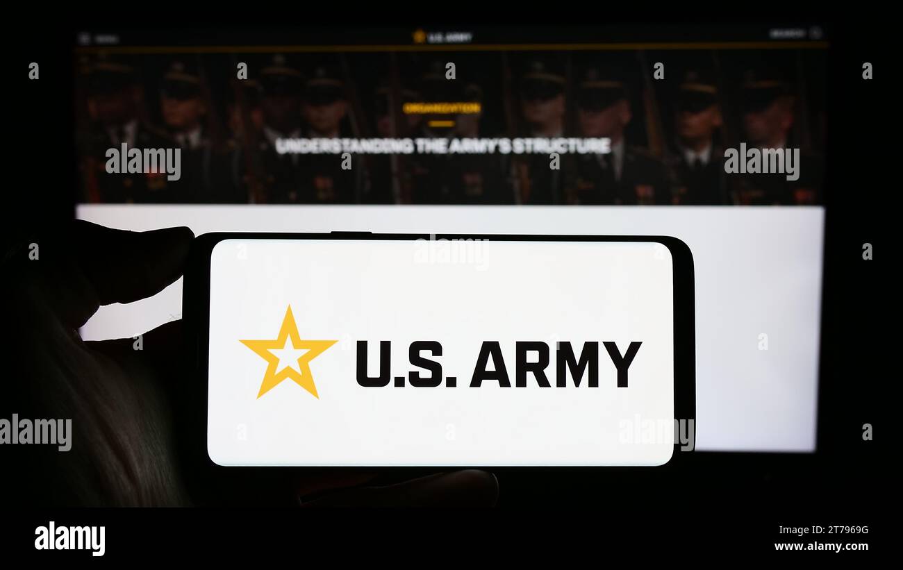 Persona che tiene il cellulare con il logo dell'esercito degli Stati Uniti davanti alla pagina Web. Concentrarsi sul display del telefono. Foto Stock